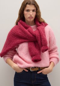 Maglione rosa a maglia con una texture morbida, abbinato a un foulard rosa scuro con dettagli a coste. Indossato con jeans blu e una cintura marrone.