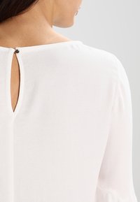 Vit blus med rund halsringning, nyckelhål på baksidan med knappstängning och mjukt, lättviktsmaterial.