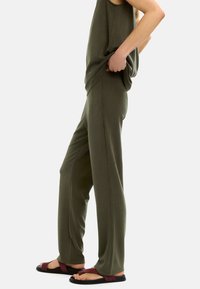 Olive green, luźna koszulka na ramiączkach zestawiona z dopasowanymi, szerokimi spodniami, wykonanymi z miękkiego materiału. Czarne sandały z burgundowymi paskami.