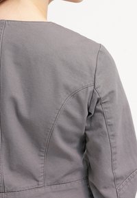 Blusa de algodón gris con un escote redondeado, costuras de hombro cosidas y una textura suave, con un diseño ajustado en la cintura.