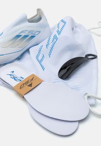 Pantofi sport albi cu accente albastre, însoțiți de tălpi interioare, o geantă albă cu șnur și un coș de pantofi negru. Texturi netede și design elegant.