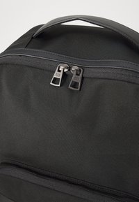 Black backpack featuring a durable textured material, dual metal zippers with a sleek pull, and a padded top handle for easy carrying.
