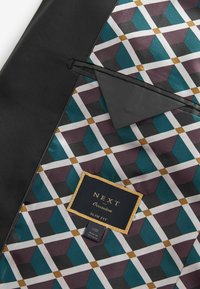 Slim-Fit-Anzugjacke mit schwarzem Äußeren. Das Innere hat ein geometrisches Muster in Teal, Burgunderrot, Grau und Weiß. Markenetikett sichtbar.