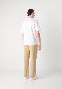 Hvit kortermet t-skjorte kombinert med beige bukser. Stoffet ser glatt ut, og antrekket fullføres med hvite sneakers.