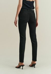Černé skinny džíny z denimu s mírně vysokým pasem, pěti kapsami a hladkým povrchem. V kombinaci s černými otevřenými lodičkami.