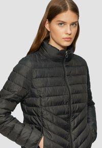 Schwarze Daunenjacke mit hohem Kragen, Reißverschluss und horizontalem Steppmuster mit diagonalen Akzenten auf der unteren Vorderseite.