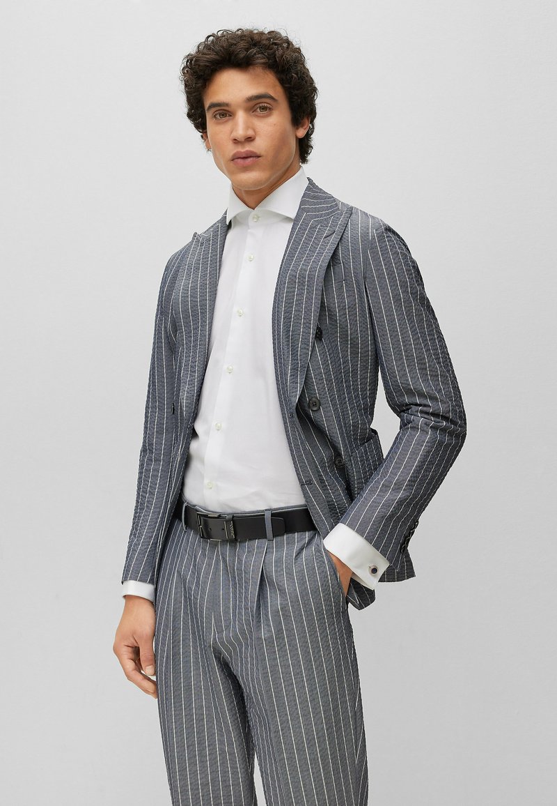 Gray pinstripe suit made of textured fabric, featuring a double-breasted jacket, white shirt, and black belt, showcasing sharp collar and cuffs.