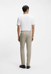 Biała krótka koszulka polo z kontrastowym wykończeniem, zestawiona z jasnobeżowymi spodniami i czarnymi butami, widziana od tyłu. Gładka faktura tkaniny.