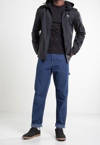 Svart, lätt zip-up jacka med huva, kombinerad med en åtsittande svart tröja och blå lösa jeans. Svarta sneakers fulländar looken.