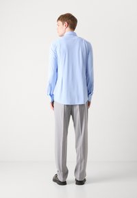 Camisa azul claro de mangas largas y puños abotonados, acompañada de pantalones gris claro. Tejido suave y corte ajustado.