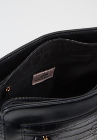 Schwarze strukturierte Handtasche aus krokodilprägtem Kunstleder mit goldenen Hardware-Akzenten und einem gefütterten Innenraum, der ein Reißverschlussfach enthält.