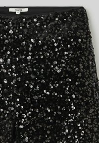 Pantalons noirs à sequins avec une texture lisse, présentant un design ajusté et une ceinture. Les sequins sont de forme circulaire et réfléchissent la lumière.