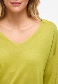 Lässiges, V-Ausschnitt-Oberteil in leuchtendem Limettengrün, aus strukturiertem Strickstoff, mit überschnittenen Schultern und minimaler Detailgestaltung.