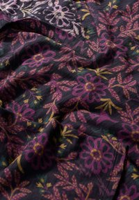 Schwarzer Stoff mit lila, gelben und grünen Blumenmustern; verfügt über eine texturierte Webart und ein V-förmiges Ausschnittdetail.