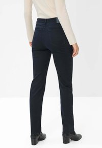 Dunkelblaue Slim-Fit-Jeans aus Denim, mit mittelhohem Bund, Gesäßtaschen und einer glatten, strukturierten Oberfläche. Kombiniert mit schwarzen Stiefeln.