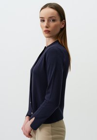 Dunkelblauer Cardigan mit langen Ärmeln, rundem Ausschnitt und goldenen Knopfdetails. Weiche Textur und schlankes Design.