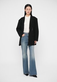 Černý volný blejzr s vykrojenými klopami, bílá košile na zapínání na knoflíky a rozšířené modré džíny. Kompletní outfit doplňují černé lodičky.