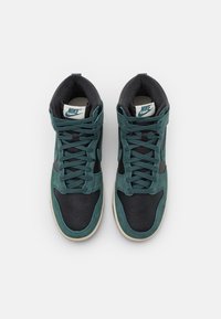Korkeat Nike-tennarit, joissa on teal-värinen mokkanahka yläosa, mustat nahkakoristeet ja reikäpohja. Nauhaverhoilu erottuvalla logolla.