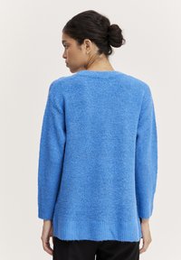 Pösig blå tröja med långa ärmar och rundad halsringning. Har ribbad fåll och detaljer på ryggen för textur.