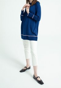 Maglione blu marina con accenti rosa all'orlo e ai polsini, abbinato a pantaloni bianchi alla caviglia e ballerine nere. Il maglione ha una vestibilità comoda.