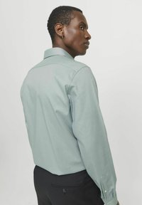 Lichtgroen, shirt met lange mouwen en een knoopsluiting-kraag, met een subtiele textuur. Heeft een schouderpasontwerp aan de achterkant en knoopmanchetten.