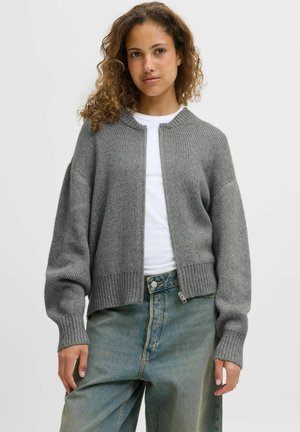 Cardigan gris en tricot avec une texture côtelée, col rond, manches longues et un ourlet ajusté et court. Porté sur un T-shirt blanc et un jean.