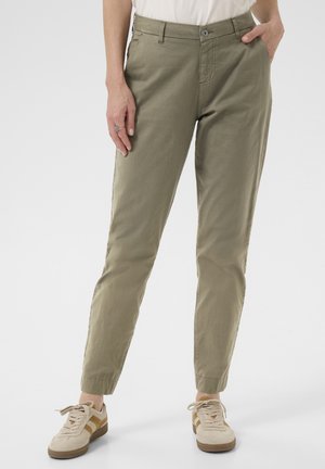 Khaki chinos with a straight fit, button closure, pockets, and ankle cuffs. Paired with cream-colored sneakers featuring light brown accents.
