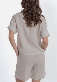 Completo in lino beige chiaro composto da una maglietta a maniche corte e pantaloni corti coordinati. Il tessuto ha una finitura texturizzata con maniche arrotolate e una vestibilità rilassata.