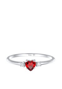 Sterling silver ring med en hjärtformad röd ädelsten i centrum, flankerat av två mindre klara stenar, polerad yta.
