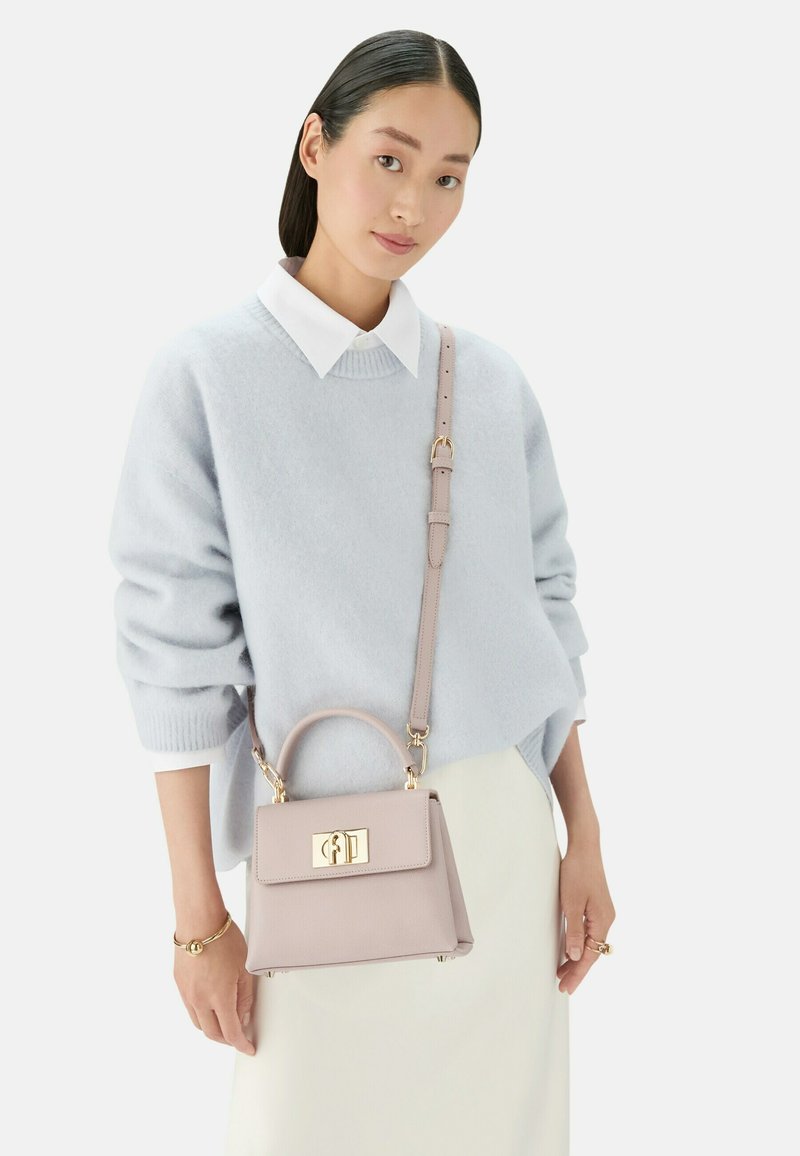 Maglione azzurro chiaro con colletto bianco, abbinato a una piccola borsa strutturata rosa pallido con hardware dorato e manico superiore.