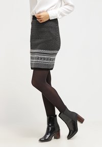 Jupe noire et blanche à motifs avec des designs géométriques au bas, portée avec des bottines noires et des collants opaques. Matière lisse, coupe ajustée.