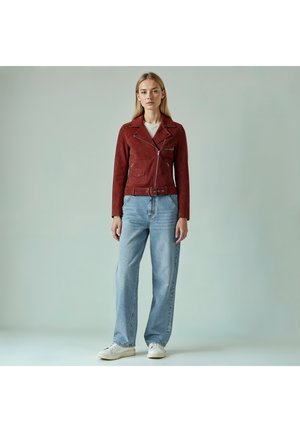 Veste de motard en daim rouge avec une taille ceinturée, des poches zippées et un col cranté, associée à un jean large bleu clair et des baskets blanches.