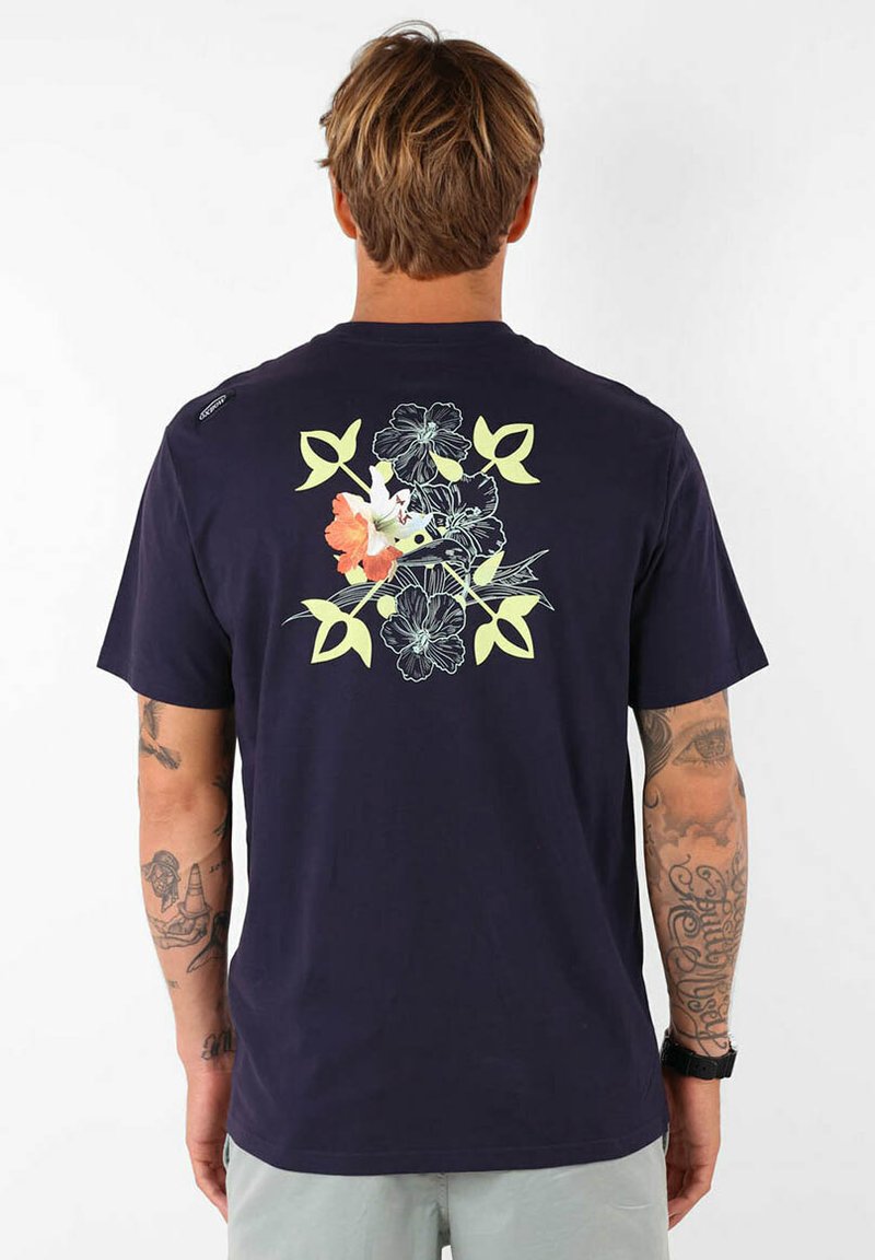 T-shirt en coton bleu marine avec un motif floral en vert clair, orange et blanc au dos. Manches courtes, col rond, coupe décontractée.