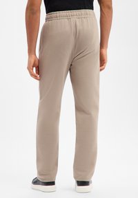 Beige Jogginghose mit entspannter Passform, elastischem Bund und glatter Textur, kombiniert mit schwarzen Slip-On-Schuhen, von hinten gezeigt.