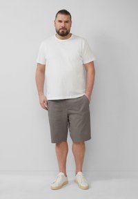 Herenoutfit bestaande uit een effen wit katoenen T-shirt, grijze katoenen shorts en witte sneakers met beige zolen; simpel, casual ontwerp.