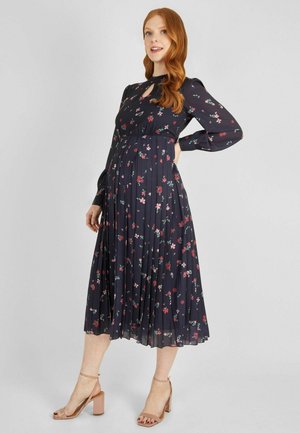 Dark floral midi dress featuring long sleeves, pleated skirt, keyhole neckline, and a fitted bodice. Accented with small, colorful flowers.