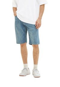 Pantalones cortos de mezclilla azul claro con un ajuste relajado, que presentan un dobladillo recto y un diseño de cinco bolsillos, combinados con una camisa blanca y zapatillas blancas.