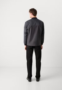 Gray jacket with a patterned upper back, long sleeves, and elastic cuffs, paired with black trousers and shoes. Minimalist design.