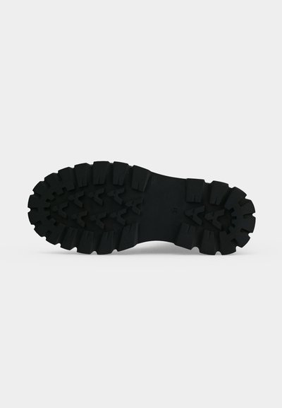 Semelle de botte en caoutchouc noir avec un motif de bande de roulement profond et robuste conçu pour la traction, présentée sur un fond clair uni.