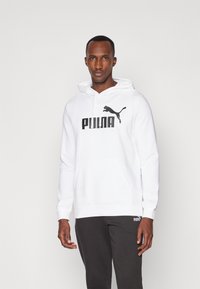 Hvid hættetrøje med en frontlomme og snøre, prydet med et sort "PUMA" logo og katte-silhuet. Sammen med mørkegrå sweatpants.
