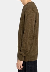 Brązowy sweter z dzianiny o fakturowanym wykończeniu, okrągłym dekoltem i długimi rękawami, prezentowany na modelce z profilu na neutralnym tle.