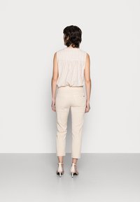 Top sin mangas de cuadros claros en crema y marrón con la parte trasera fruncida; combinado con pantalones ajustados crema y tacones beige con tiras.