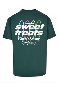 Grøn bomulds t-shirt med et grafisk tekstdesign i hvid, pink og gul: "UPSCALE sweet treats Candy's Loving Symphony" på ryggen.