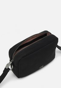 Czarna syntetyczna torebka na ramię o prostokątnym kształcie, zamykana na górny suwak, z gładką teksturą. Posiada subtelny srebrny akcent oraz podszycie wewnętrzne.