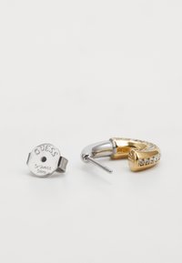 Srebrne i zlatne kružne naušnice; srebrna ima ugravirano "GUESS Stainless Steel". Zlatna sadrži prozirne rhinestone kamenčiće duž prednjeg ruba.