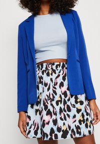 Blå blazer över en ljusblå ribbad crop top, i kombination med en kjol med en pastellblå bakgrund och svarta, rosa och beige leopardmönster.