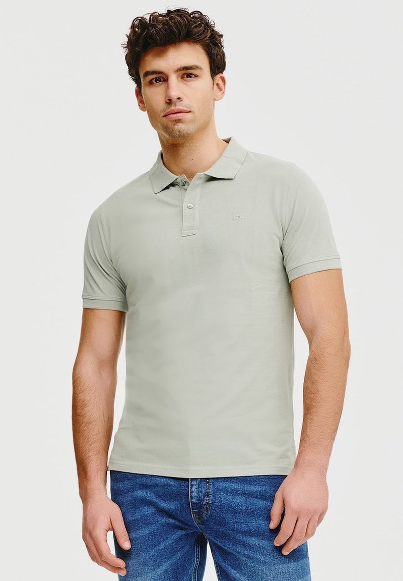 Koszulka polo w jasnym zielonym kolorze, wykonana z bawełny, z kołnierzykiem, dwoma guzikami i krótkimi rękawami. Noszona z niebieskimi dżinsami.