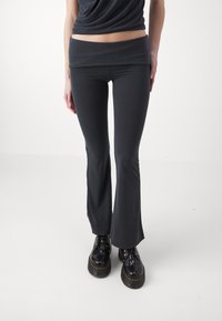Sötét szürke, lágy anyagból készült, bővülő leggings, széles, behajtható derékpánttal, fekete platform cipőkkel párosítva.
