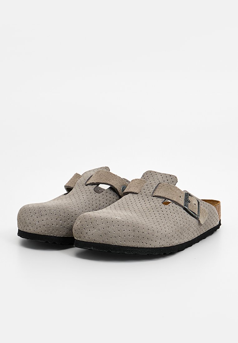 Graue, perforierte Clogs zum Hineinschlüpfen mit einem Korkfußbett, verstellbarem Riemen und einer schwarzen Gummisohle. Sie zeichnen sich durch eine glatte Textur und ein klassisches Design aus.