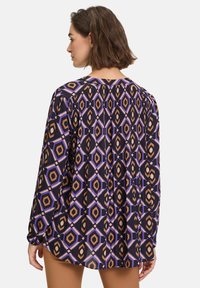 Long-sleeve blouse in lightweight fabric features a geometric pattern with hexagons in purple, orange, and black, gathered back detail.